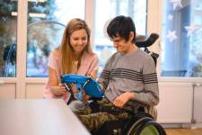 Ein Mann im Rollstuhl bedient ein Tablett. Neben ihm sitzt eine Frau. 