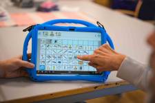 Eine Hand tippt auf ein Tablett mit Metacom Symbolen.