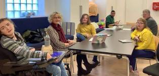 Zwei Klienten des slw sitzen  am Tisch vor einem Tablett gemeinsam mit einer Mitarbeiterin der Lebenswelt-Tirol-Sprachwerkstatt. 