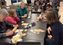 Sechs Personen sitzen am Tisch, darunter Klienten des slw sowie Unterstützer und rollen Keksteig aus. 