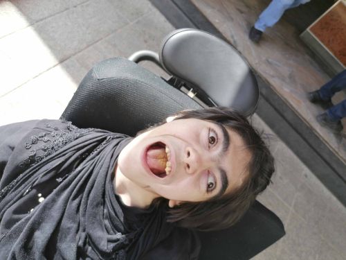 eine Frau mit Behinderung sitzt im Rollstuhl und lächelt