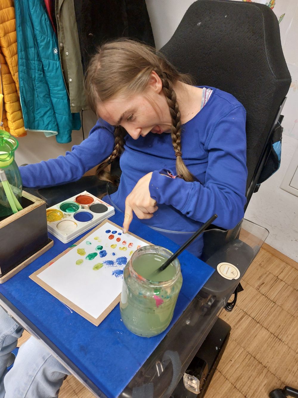 eine Frau im Rollstuhl zeichnet mit Fingerfarben auf einem Blatt Papier