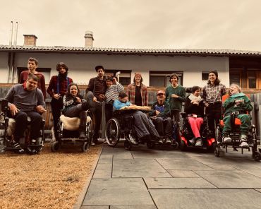 ein Gruppenbild von mehreren Erwachsenen mit Behinderungen und ihren Unterstützer_innen; einige sitzen im Rollstuhl; Aufnahme im Freien