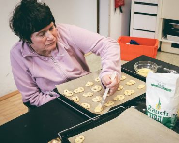 eine frau pinselt Ei auf kleine Brezen auf dem Backblech