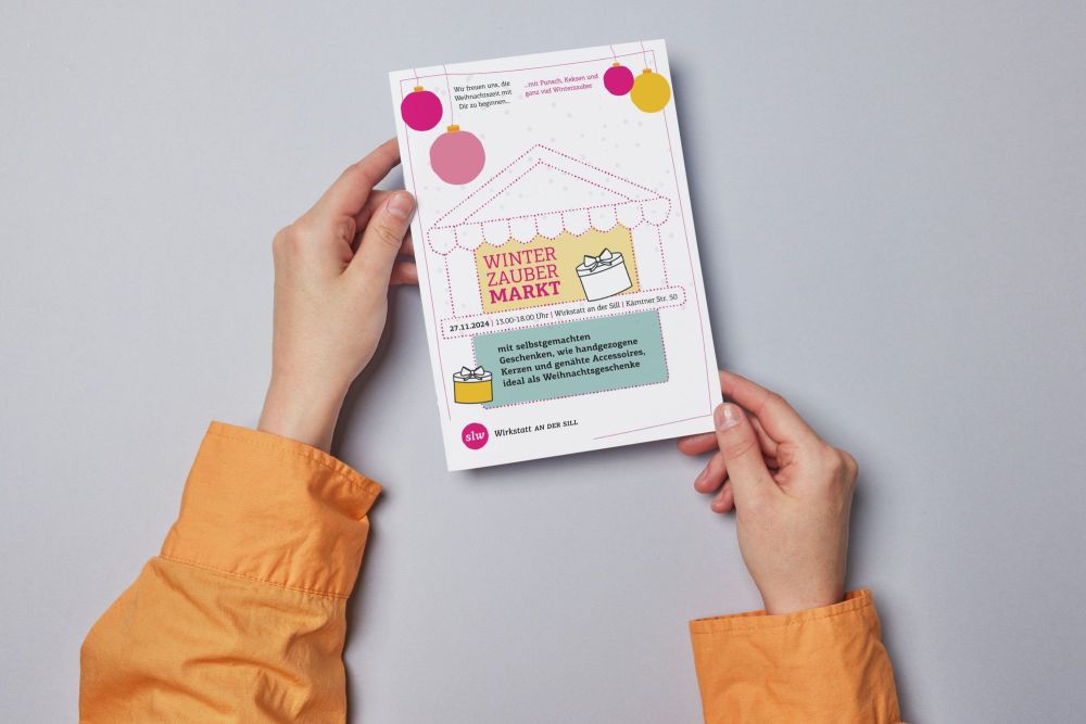 zwei Hände halten einen Flyer; auf dem Flyer ist eine Einladung zum Winterzaubermarkt am 27.11.2024