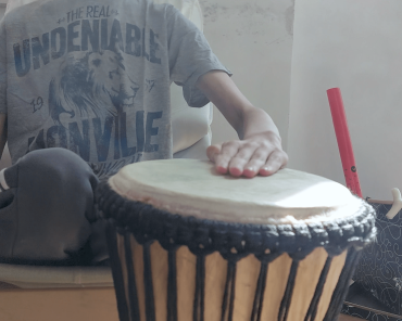 jemand sitzt auf einem Stuhl und die flache Hand liegt auf einer Trommel