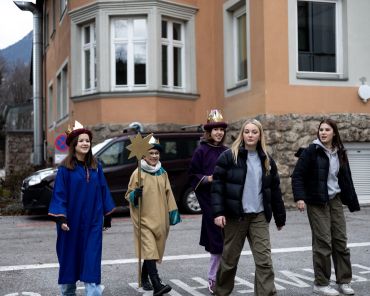 drei Sternsinger spazieren mit zwei Begleitpersonen über einen Parkplatz