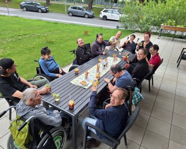 eine Gruppe von Menschen mit Behinderungen sitzen um einen Tisch auf der Terrasse; vor ihnen stehen alkoholfreie Cocktails