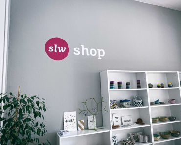 eine graue Wand, darauf steht slw Shop, ein paar Regale mit Dingen darin