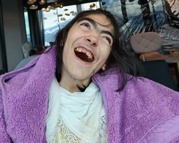 eine Frau mit Behinderung lächelt mit einem rosa Handtuch um die Schultern