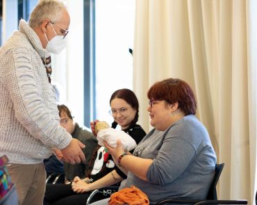 ein Mann gibt einer Frau mit Behinderung eine Puppe in den Arm
