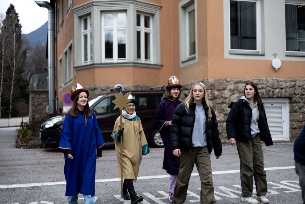 drei Sternsinger spazieren mit zwei Begleitpersonen über einen Parkplatz