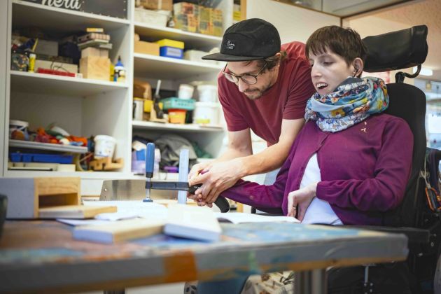 ein Unterstützer und ein Mann mit Behinderung halten kleine Topfpflanzen im Garten der Wirkstatt Axams