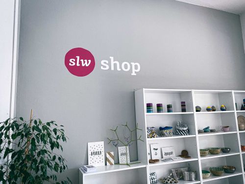 eine graue Wand, darauf steht slw Shop, ein paar Regale mit Dingen darin
