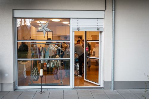 ein Foto von außen von einer Fensterscheibe. im Haus sieht man Produkte und viele Menschen