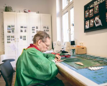 ein Mann mit einer grünen Malerschürze bemalt kleine Weihnachtsbäume aus Holz