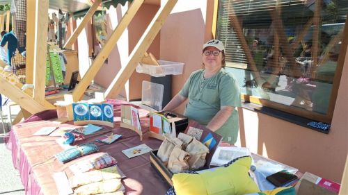 ein Mann mit Downsyndrom steht vor einem Marktstand mit verschiedenen Produkten und lächelt in die Kamera