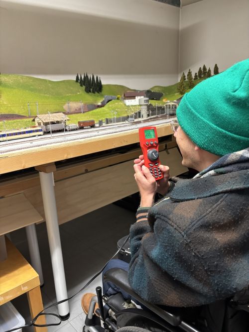ein Mann im Rollstuhl mit Mütze bedient eine Fernbedienung für die Modelleisenbahn