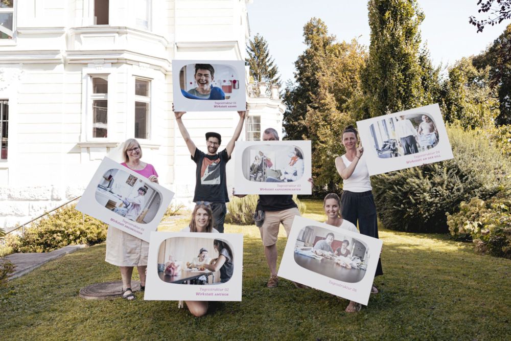 sechs Erwachsene stehen auf einer Wiese und halten Tafeln mit Bildern in die Luft