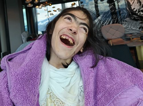 eine Frau mit Behinderung lächelt mit einem rosa Handtuch um die Schultern