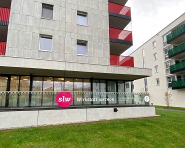 ein Hochhaus mit Grünfläche davor; auf der Glasfläche der Terrassenbegrenzung steht slw Wirkstatt Amthor
