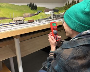 ein Mann im Rollstuhl mit Mütze bedient eine Fernbedienung für die Modelleisenbahn