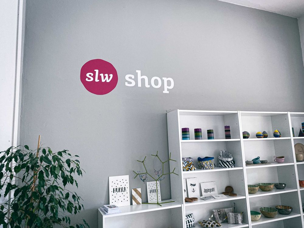 eine graue Wand, darauf steht slw Shop, ein paar Regale mit Dingen darin