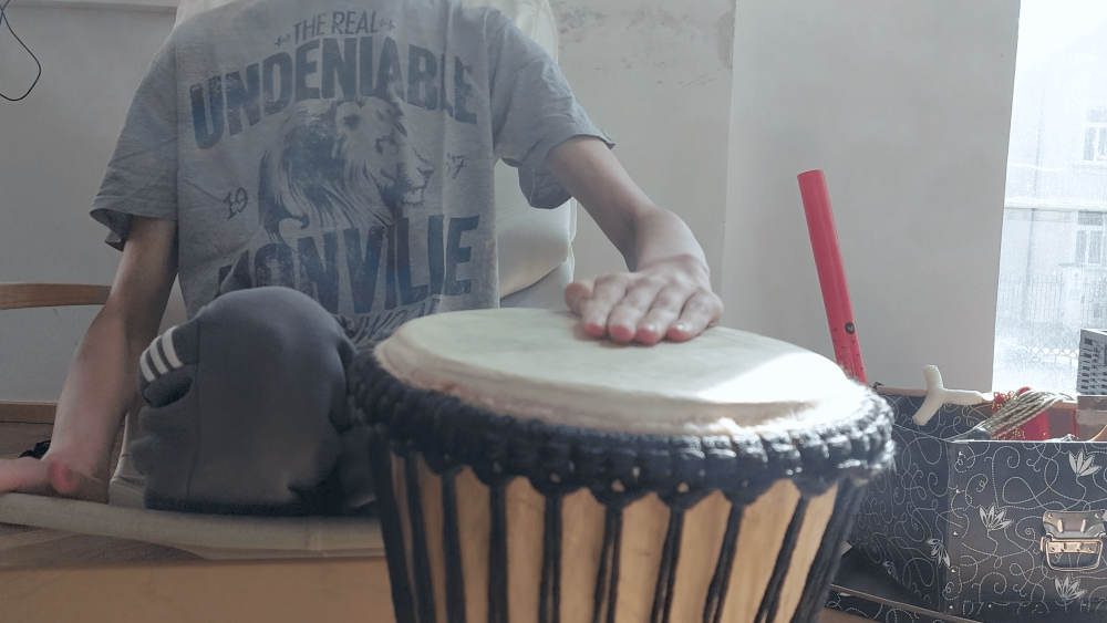 jemand sitzt auf einem Stuhl und die flache Hand liegt auf einer Trommel