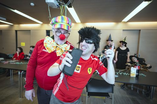 ein Mann ist als Clown verkleidet und ein anderer trägt Perücke, Sonnenbrille und Fußballtrikot; sie hören Musik