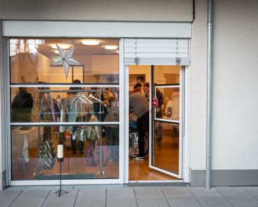 ein Foto von außen von einer Fensterscheibe. im Haus sieht man Produkte und viele Menschen