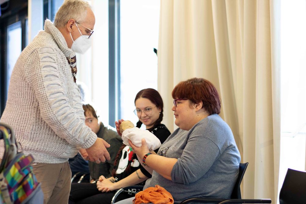 ein Mann gibt einer Frau mit Behinderung eine Puppe in den Arm