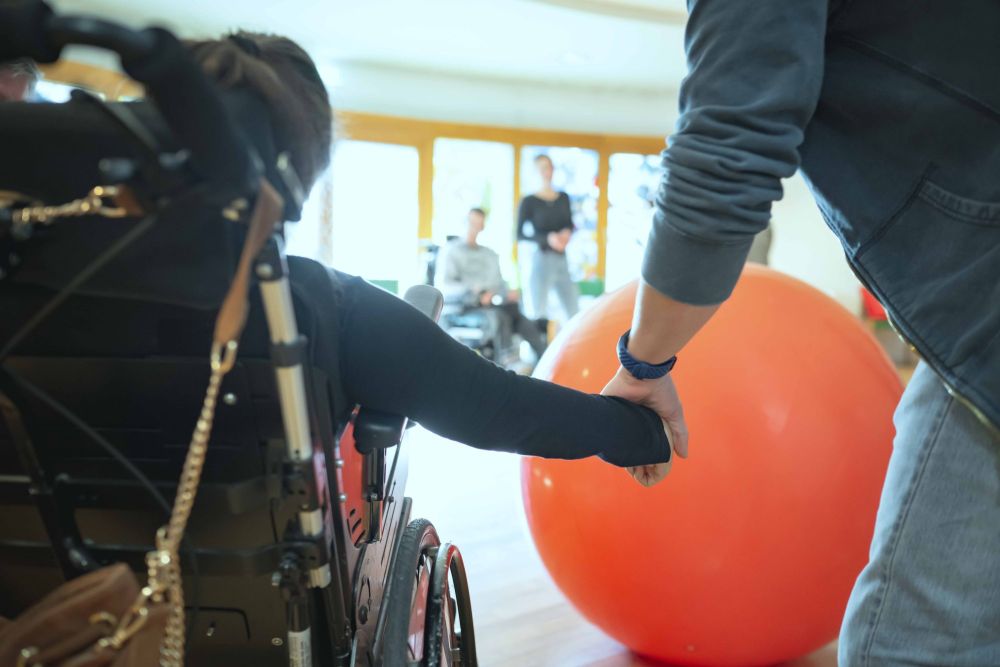 ein Mensch mit Behinderung und ein weiterer halten Hand; man sieht einen großen roten Gymnastikball