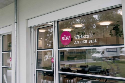 eine Fensterscheibe mit einer Beklebung: das slw Logo und "Wirkstatt an der Sill"