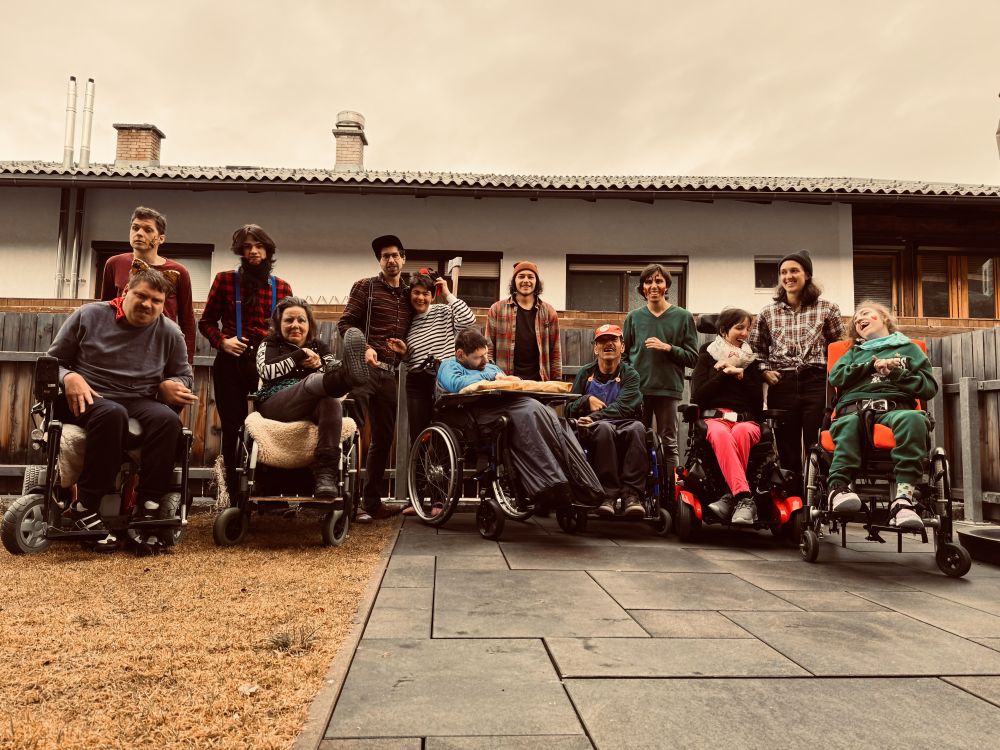 ein Gruppenbild von mehreren Erwachsenen mit Behinderungen und ihren Unterstützer_innen; einige sitzen im Rollstuhl; Aufnahme im Freien