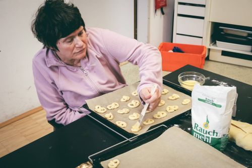 eine frau pinselt Ei auf kleine Brezen auf dem Backblech