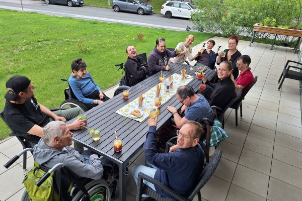 eine Gruppe von Menschen mit Behinderungen sitzen um einen Tisch auf der Terrasse; vor ihnen stehen alkoholfreie Cocktails