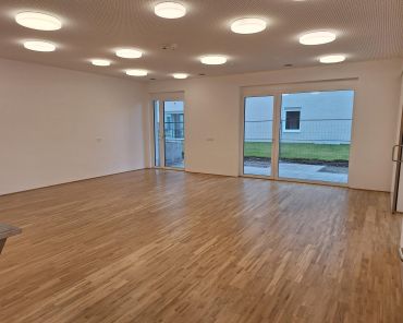 ein leerer Raum mit Holzboden, Lampen an der Decke und einer Fensterfront auf einer Wandseite