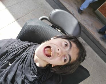 eine Frau mit Behinderung sitzt im Rollstuhl und lächelt